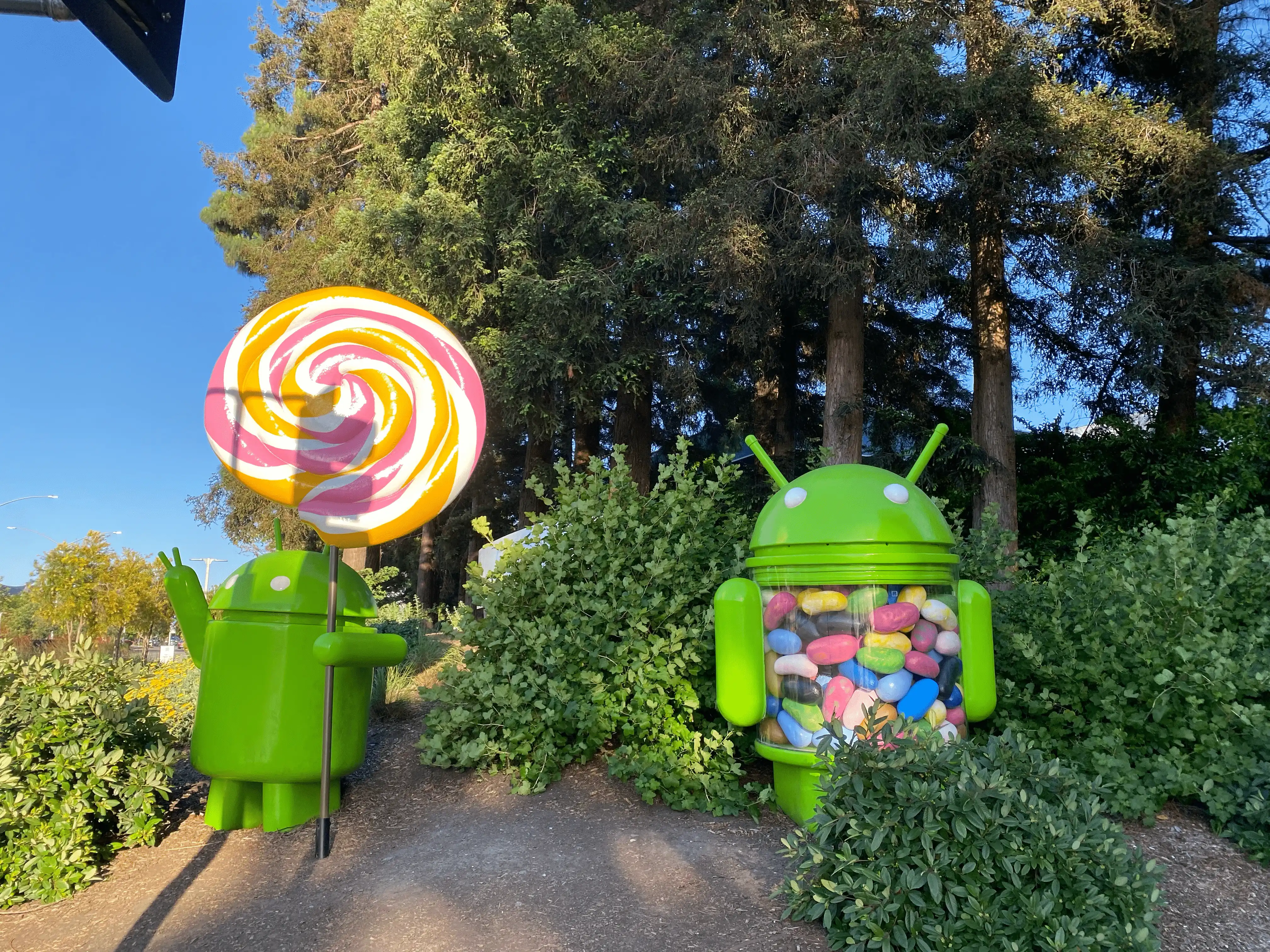 Two green Android mascot robot art objects. One is holding a lollipop, and the other has a translucent torso filled with gummy bears.