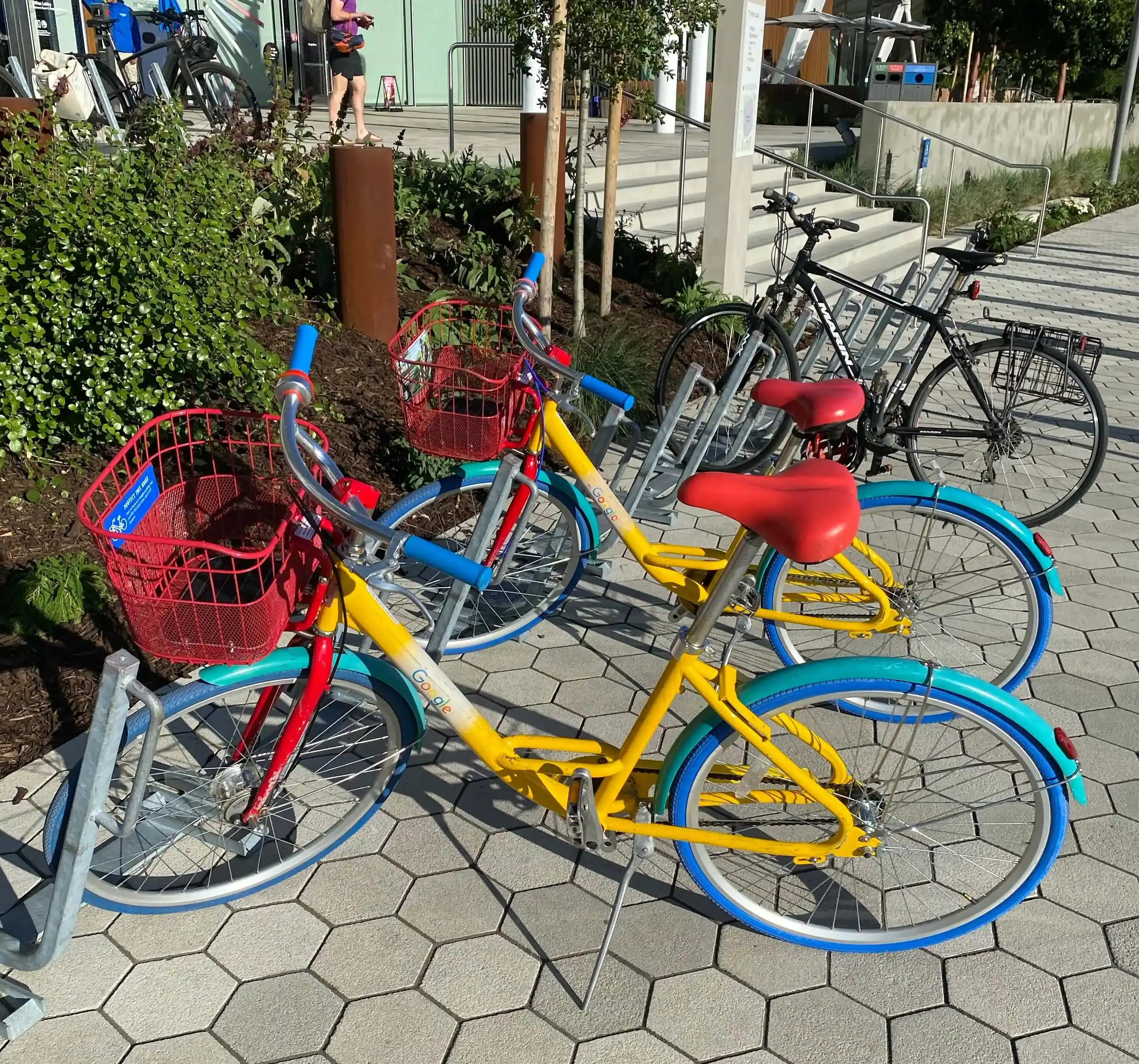 Three Google-colored bicycles, with yellow bodies, red baskets, and blue handlebars and tires, are parked