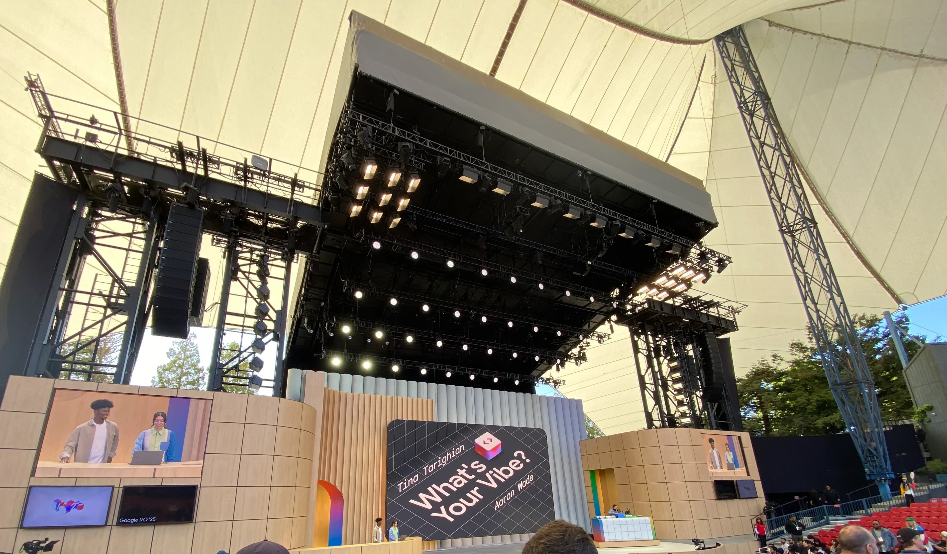 Inside the venue. There's a tent-like roof that cuts off midway, and a large screen is visible.