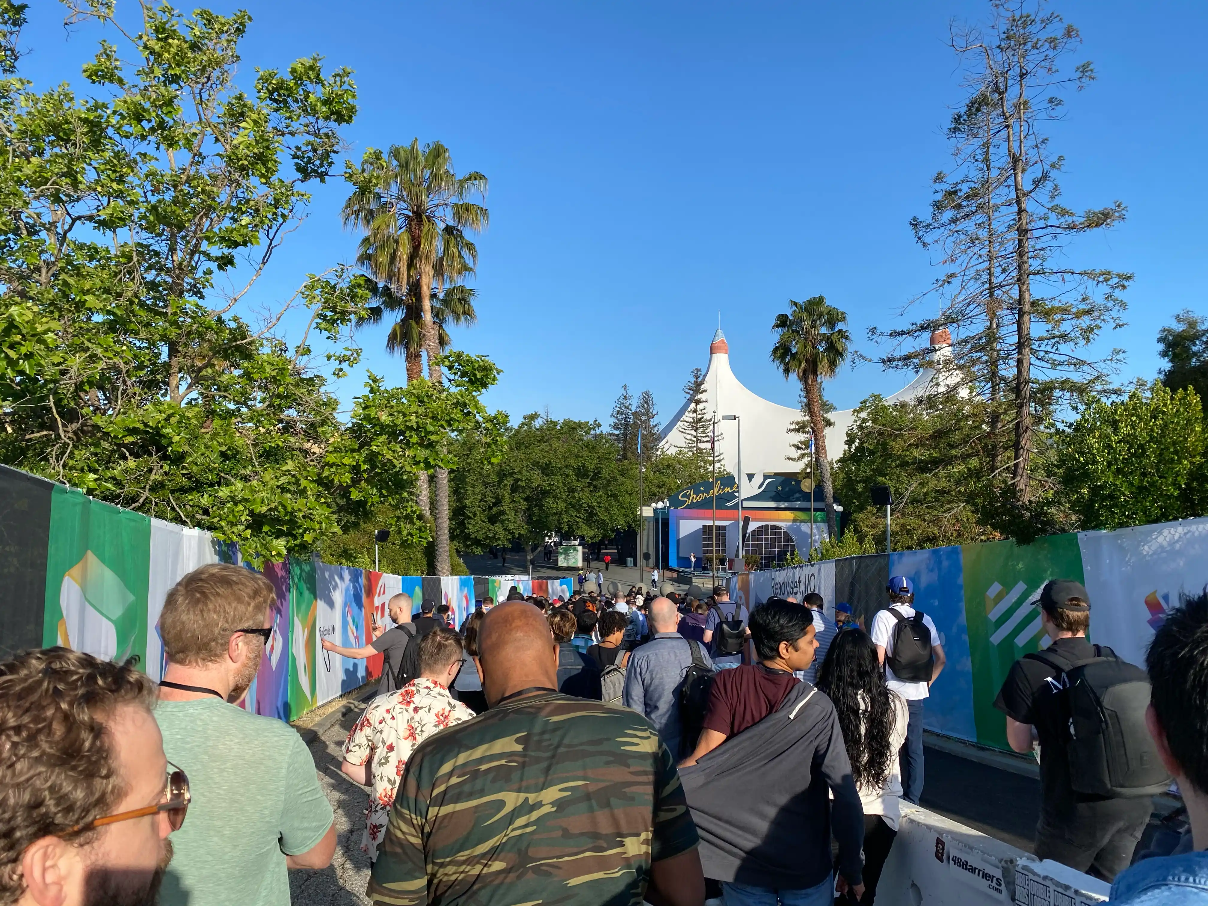 A line of people waiting for the venue to open. The top of a circus tent-like roof is visible in the distance.