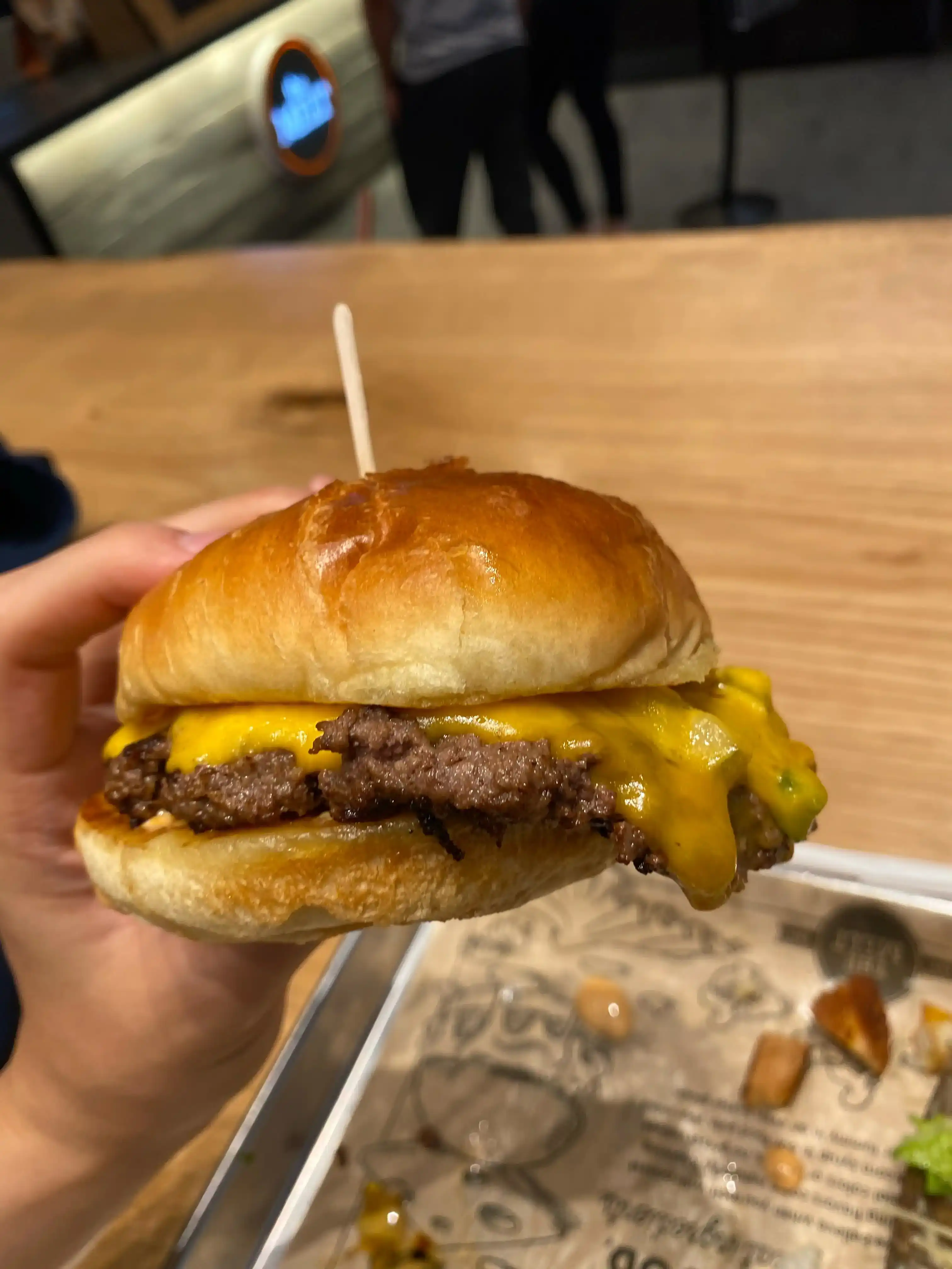 A hamburger held in a left hand. Melted cheese and a thick patty are overflowing from the bun.