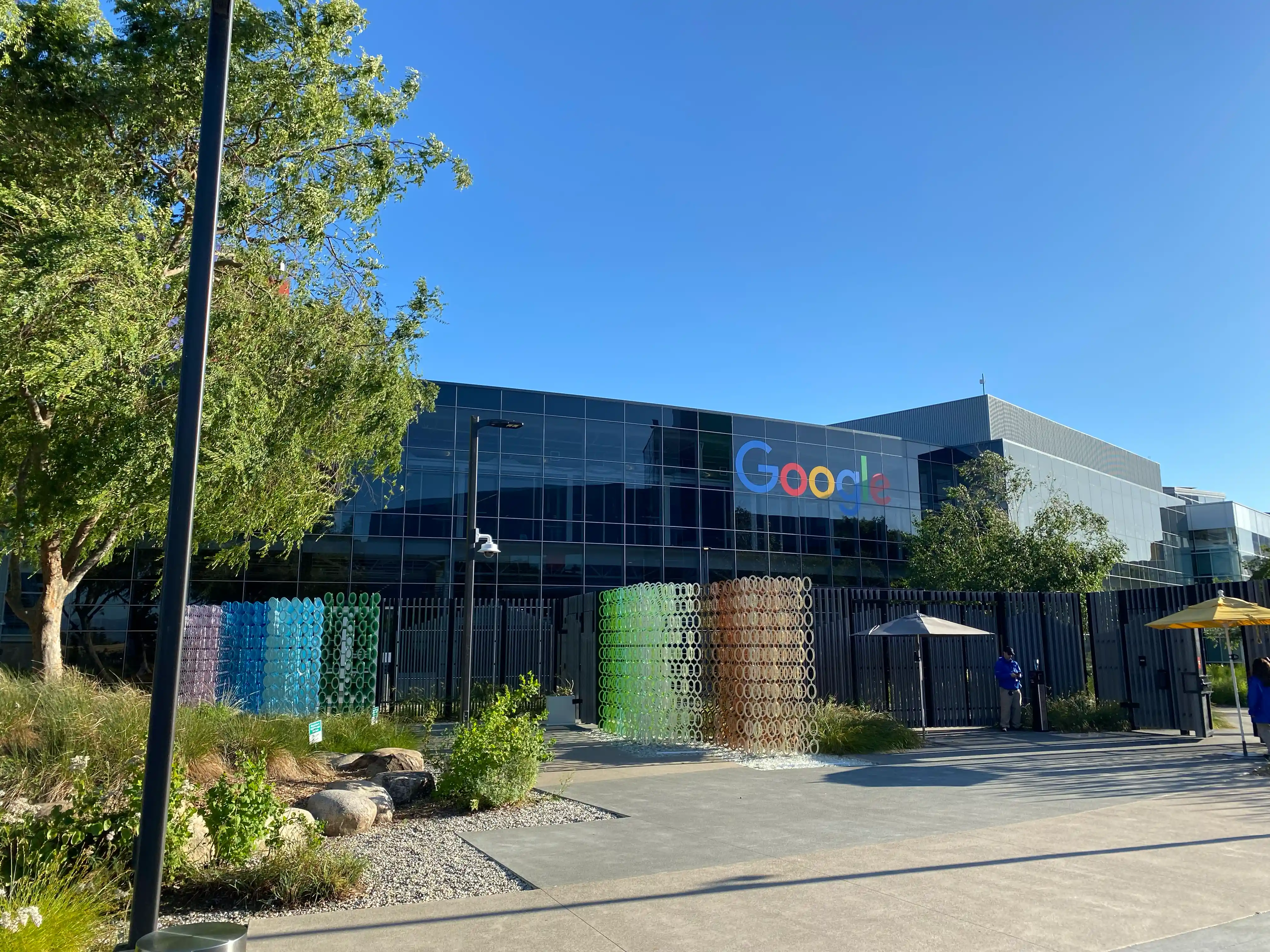 A glass-fronted office building. The Google logo is prominently displayed on the glass wall.